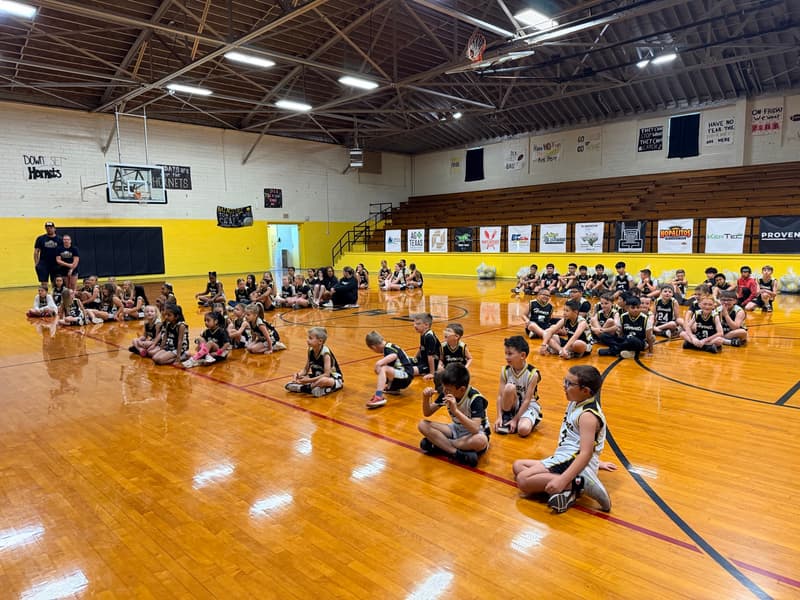 Rows of Hornets and Nettes players sitting on the gym floor, listening